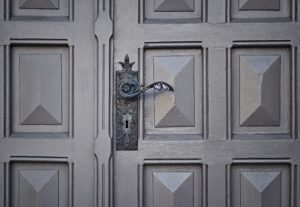A grey entry door with a intricate metal door handle.