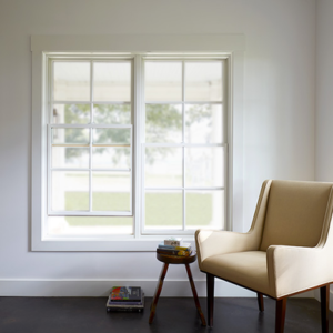 Image of the corner of a room. There is a beige chair with a small end table next to a large window.