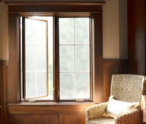 Sunlight streaming through one open and one closed casement window to the left of a single chair