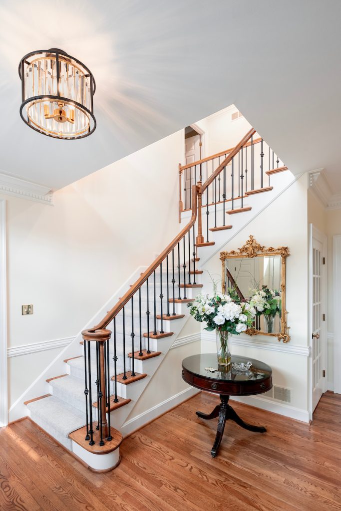 Elegant staircase with iron balusters, wood handrail, and floral entryway table