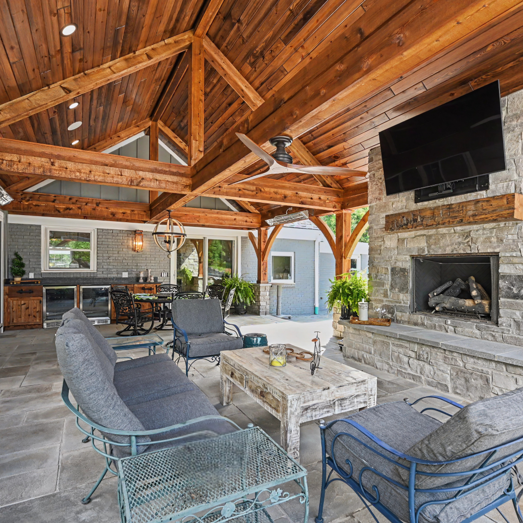 Covered outdoor living space remodel in Lexington, KY with timber beams, stone fireplace, and vaulted wood ceiling